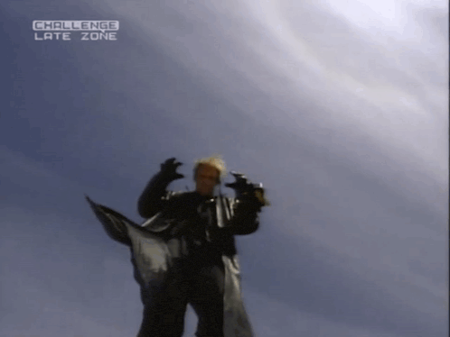 a man in a black coat stands in front of a blue sky with the words challenge late zone above him