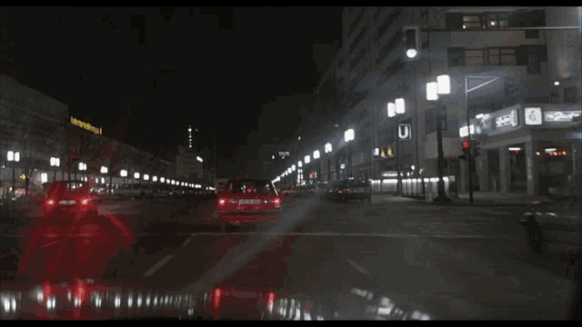 a red car is driving down a street at night with a yellow sign that says bahnhof strasse