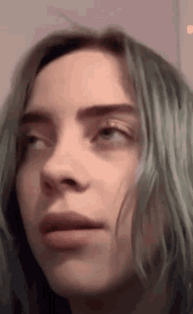 billie eilish is making a funny face with her eyes closed and her mouth open .
