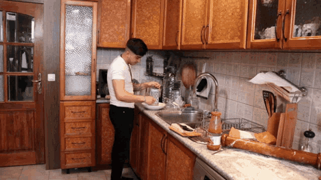 a man in a white shirt is washing dishes in a kitchen with wooden cabinets