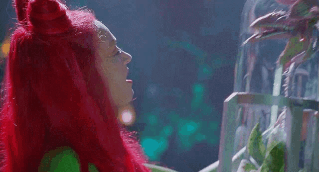 a woman with red hair and a green shirt is looking at a fish tank .