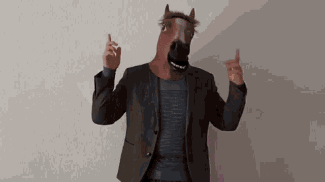 a man wearing a horse mask and a suit is making a gesture with his hands .