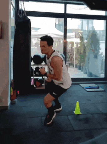a man squatting in front of a window with a boxing bag in the background