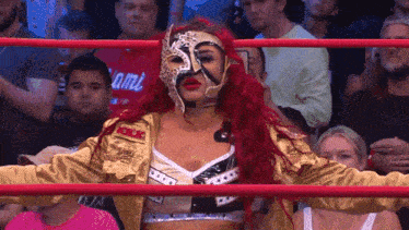 a woman in a mask stands in a wrestling ring with a crowd behind her and a shirt that says miami on it