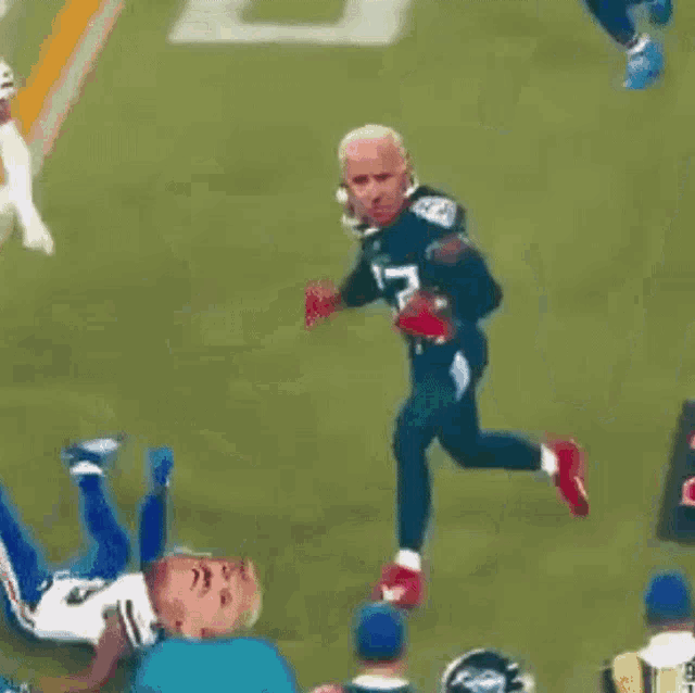 two men are running on a football field and one of them has a face on his jersey .