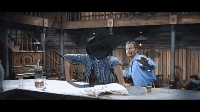 a man in a cowboy hat sits at a bar with another man pointing