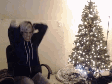 a person sitting in front of a christmas tree with their hands in the air
