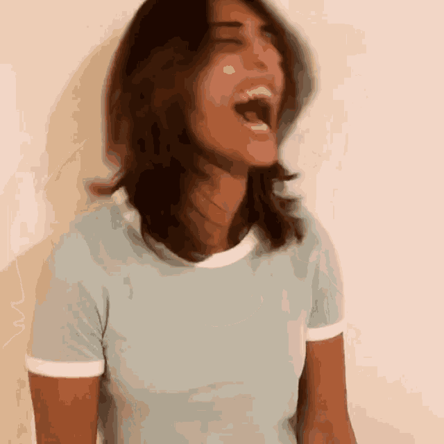 a woman in a blue shirt is laughing with her mouth wide open .