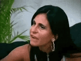 a woman is sitting on a couch making a funny face and wearing hoop earrings .