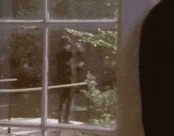 a man is standing in front of a window looking out at trees