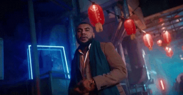 a man in a suit and scarf is standing in a dark room with chinese lanterns .