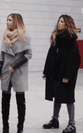 two women are standing next to each other wearing coats and boots .