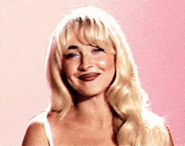 a close up of a woman 's face with blonde hair and a pink background