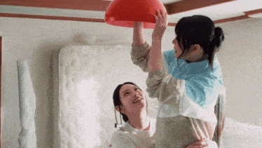 a woman in a blue jacket is holding a red ball over another woman 's head