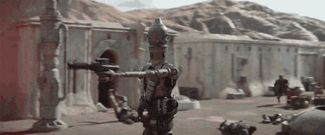 a robot is holding a gun in front of a building in the desert .