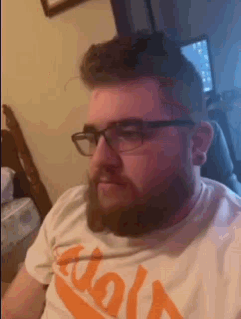 a man with a beard and glasses is wearing a white t-shirt .