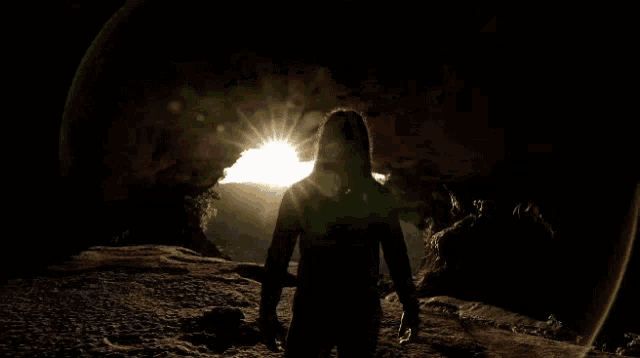 a person standing in a cave with the sun shining through