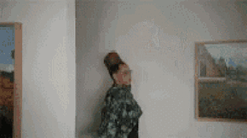 a woman is standing in a room with a bun on her head and a painting on the wall .