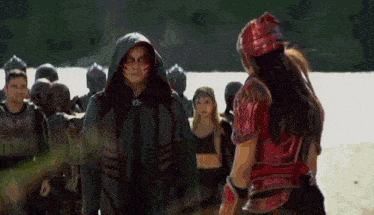 a man in a hooded jacket is standing next to a woman in armor on a beach .
