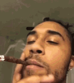 a close up of a man smoking a cigarette with his eyes closed .