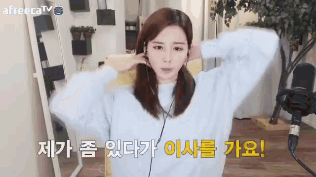 a woman wearing headphones and a blue sweater is sitting in front of a microphone and says afreecatv