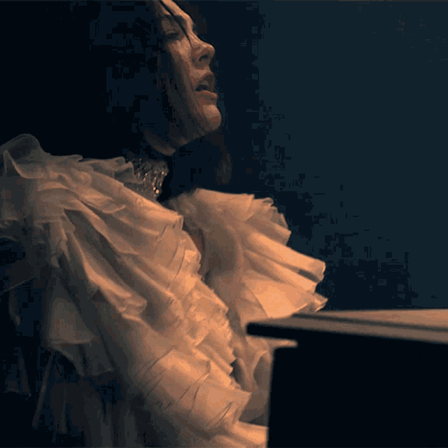a woman wearing a white ruffled top is sitting at a piano