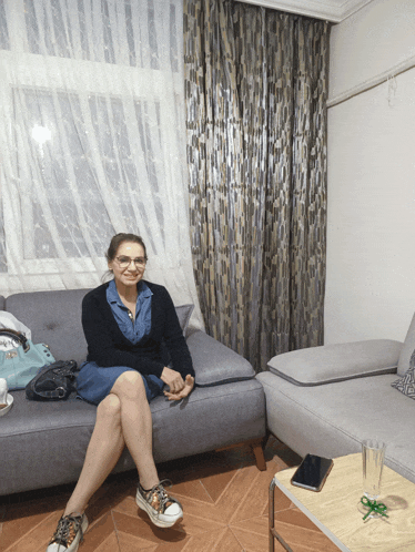 a woman sits on a couch with her legs crossed in front of a window