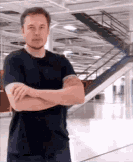 elon musk is standing with his arms crossed in front of stairs