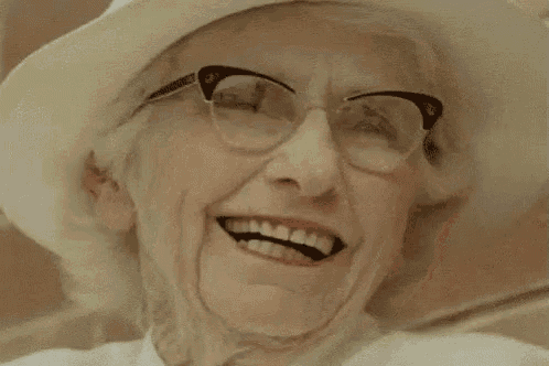an older woman wearing glasses and a white hat is smiling .