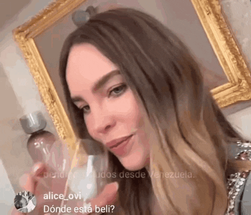 a woman is holding a glass in front of a gold framed picture ..