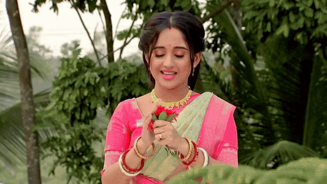 a woman in a pink top is holding a red flower in her hands
