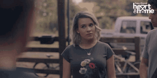 a girl in a floral shirt stands in front of a sign that says heart & home