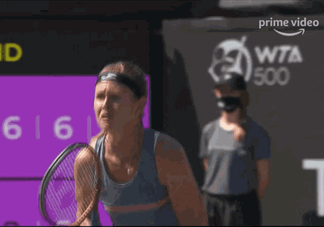 a woman is holding a tennis racquet in front of a sign that says prime video