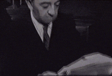 a man wearing glasses is reading a book in a dark room