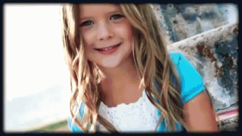 a little girl in a blue shirt is smiling and looking at the camera