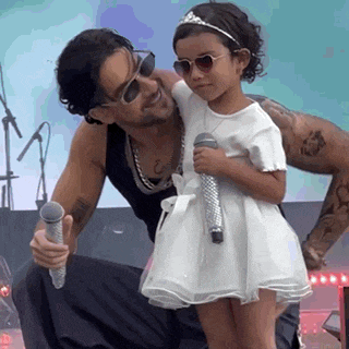 a man is holding a little girl who is wearing a tiara and sunglasses .