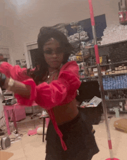 a woman in a pink crop top is holding a mop in her hand .