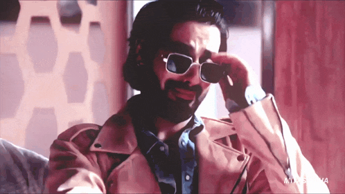 a man with a beard wearing sunglasses and a pink jacket with the word maxsoma on the bottom