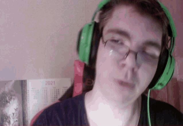 a man wearing headphones and glasses looks at the camera with a calendar behind him that says 2021