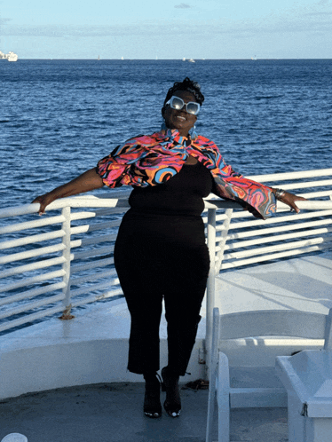 a woman wearing sunglasses and a colorful shirt is standing on a railing overlooking the ocean
