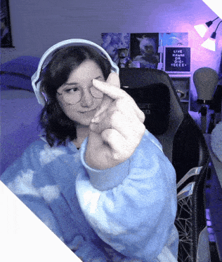 a girl wearing headphones and glasses giving the middle finger in front of a poster that says live and die yeeee