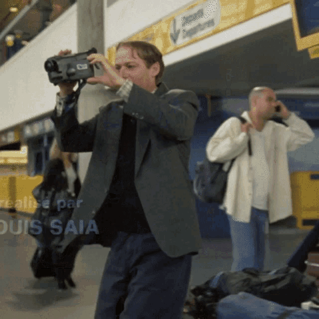 a man in a suit is taking a picture with a camera with the words realise par louis saia on the bottom right