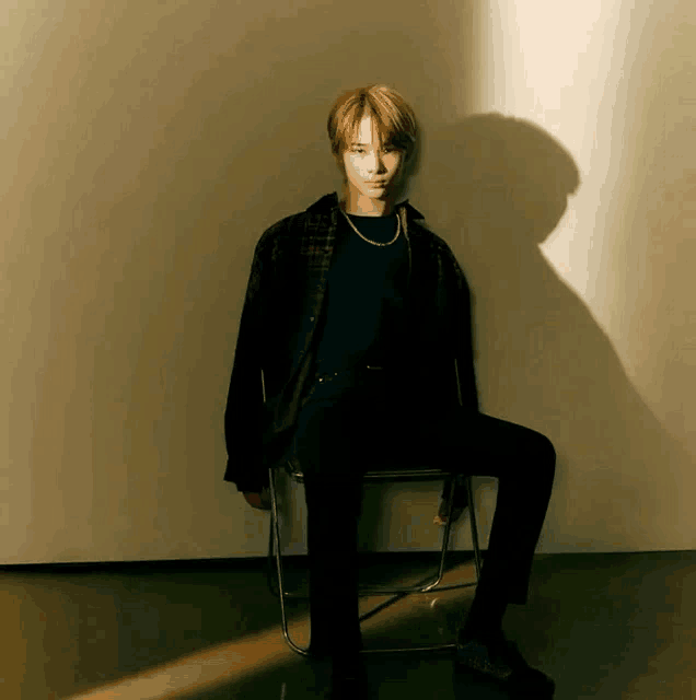 a young man is sitting on a chair with his legs crossed against a wall .