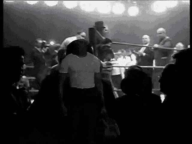 a man in a white shirt is walking into a boxing ring surrounded by people .