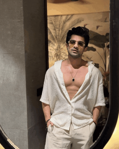 a shirtless man wearing sunglasses and a necklace is standing in front of a mirror