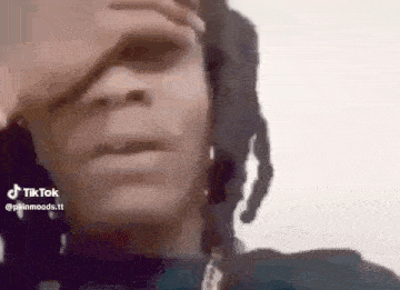 a close up of a person with dreadlocks covering their face with their hand .