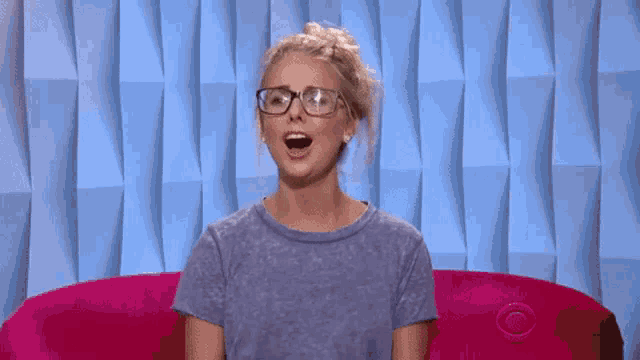 a woman wearing glasses sits on a pink couch