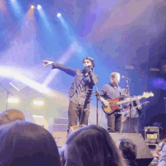 a man singing into a microphone while another man plays a guitar on stage