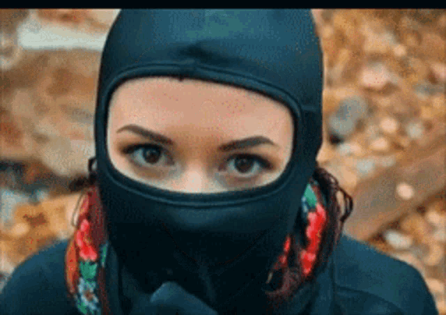 a woman wearing a balaclava covering her face looks at the camera