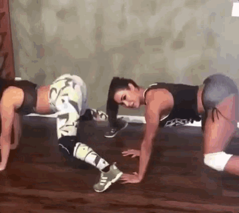 two women are doing push ups on a wooden floor in a gym .